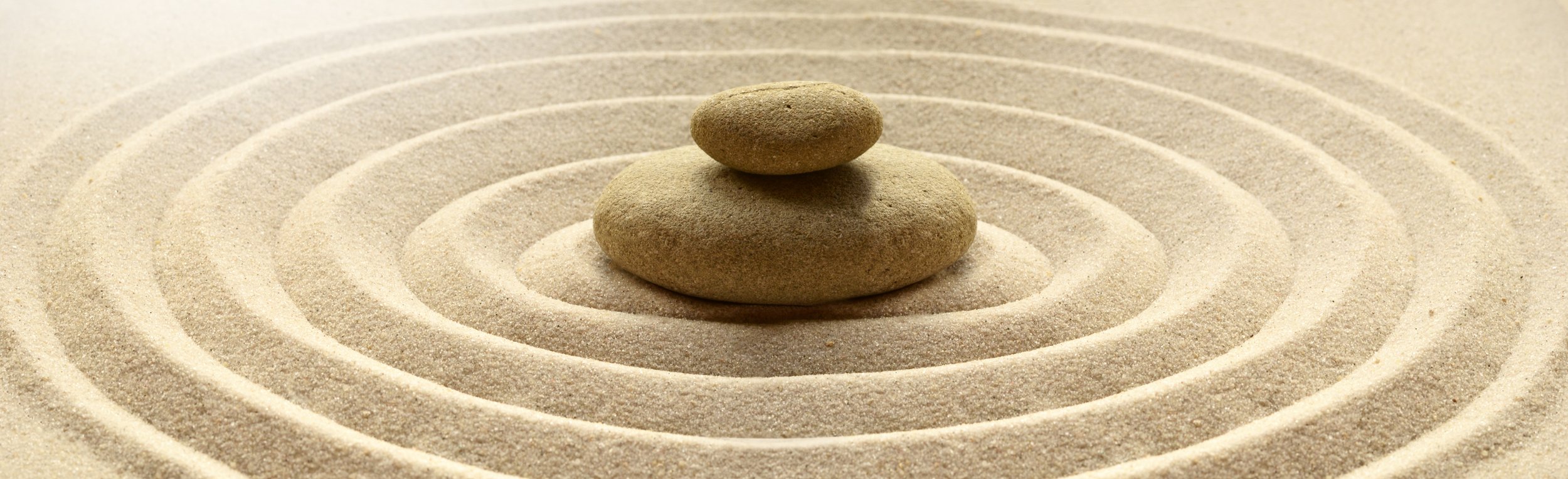Two stacked rocks on a sand Zen garden with concentric circular raked patterns.